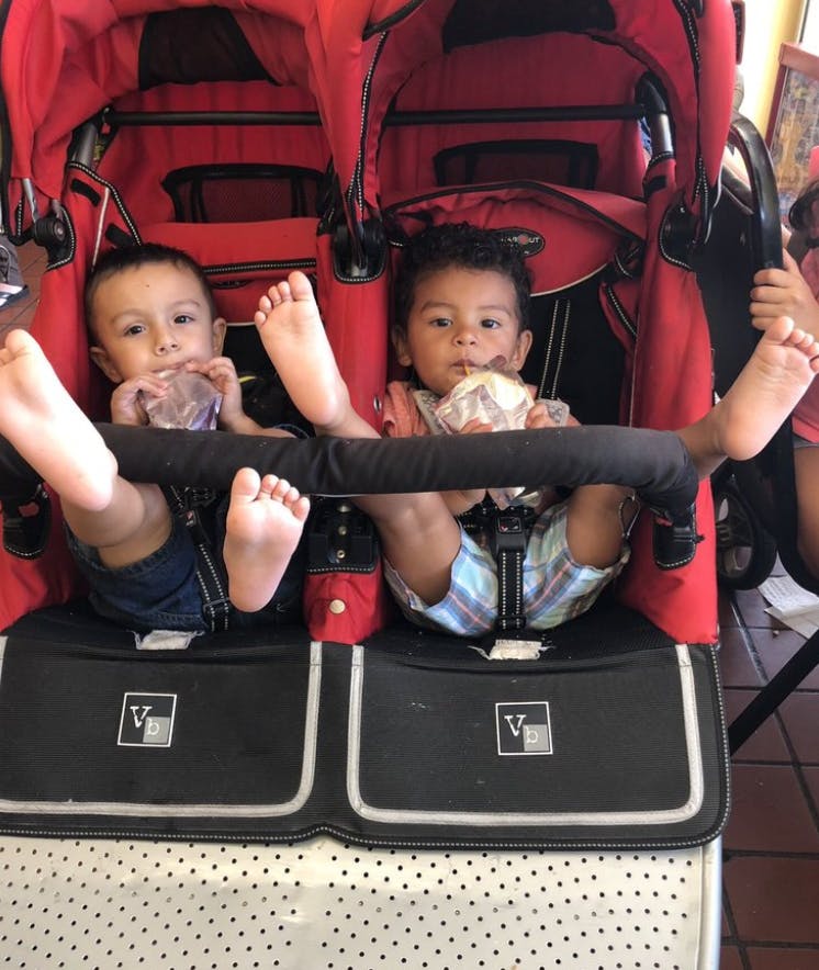 Two children sitting in a red double stroller