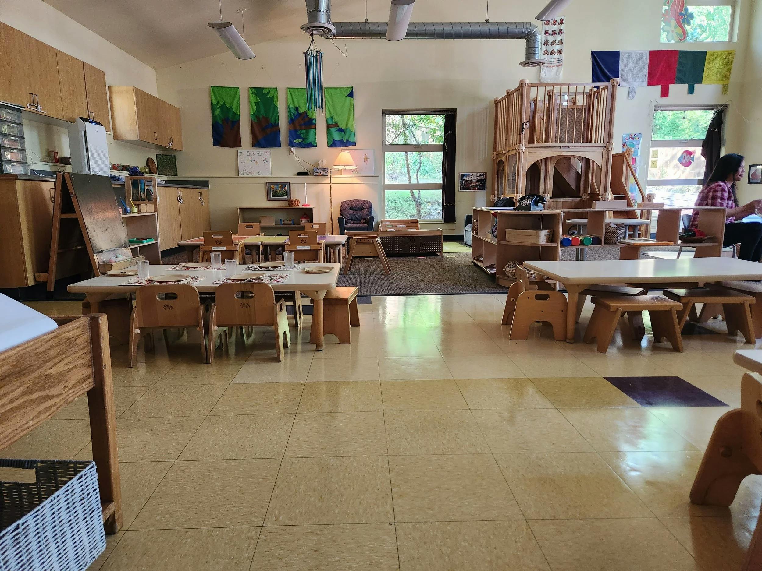 Classroom with child-sized tables and chairs, wood cabinets, and large windows