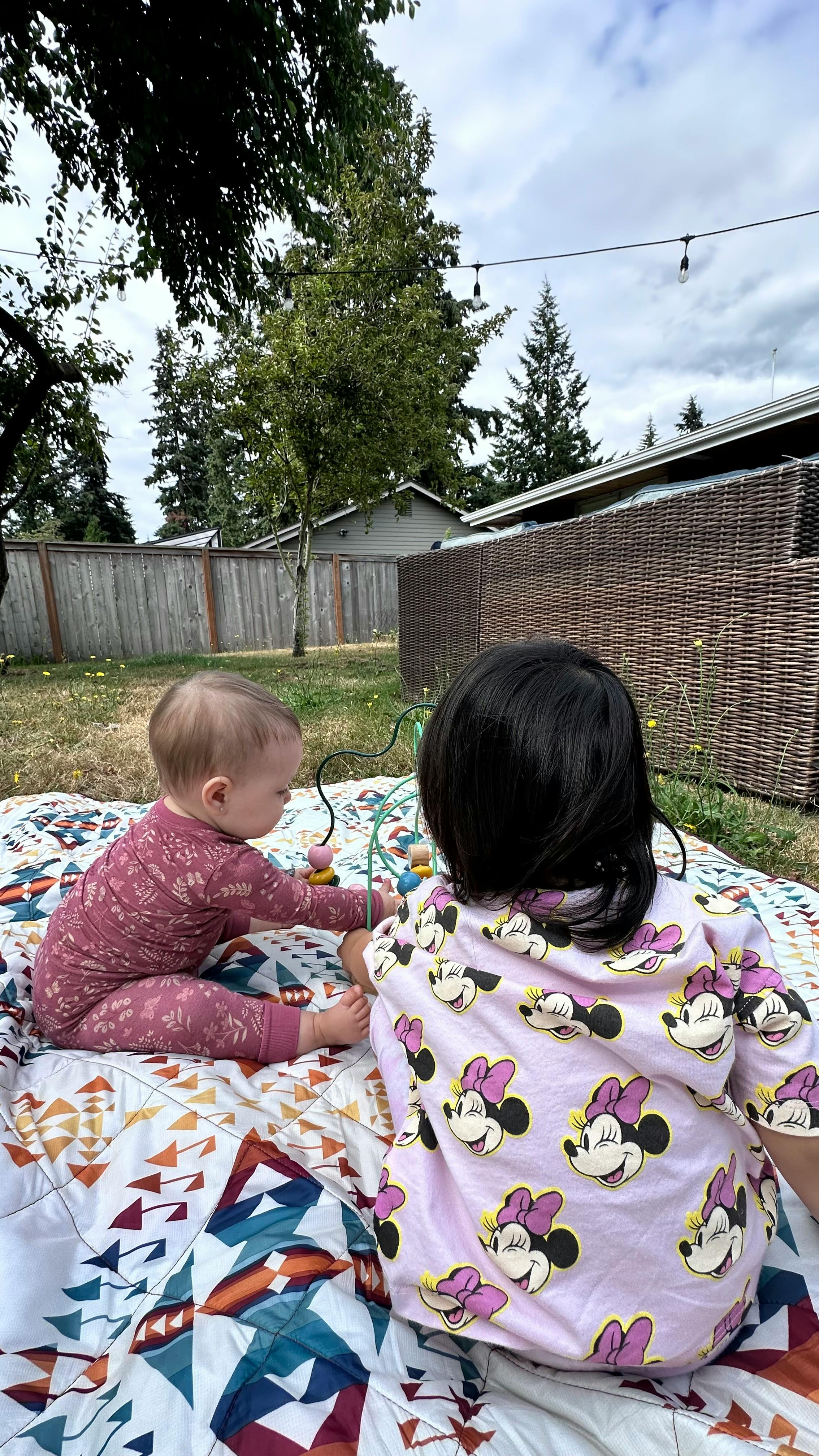 Two children playing with a toy on a blanket outdoors