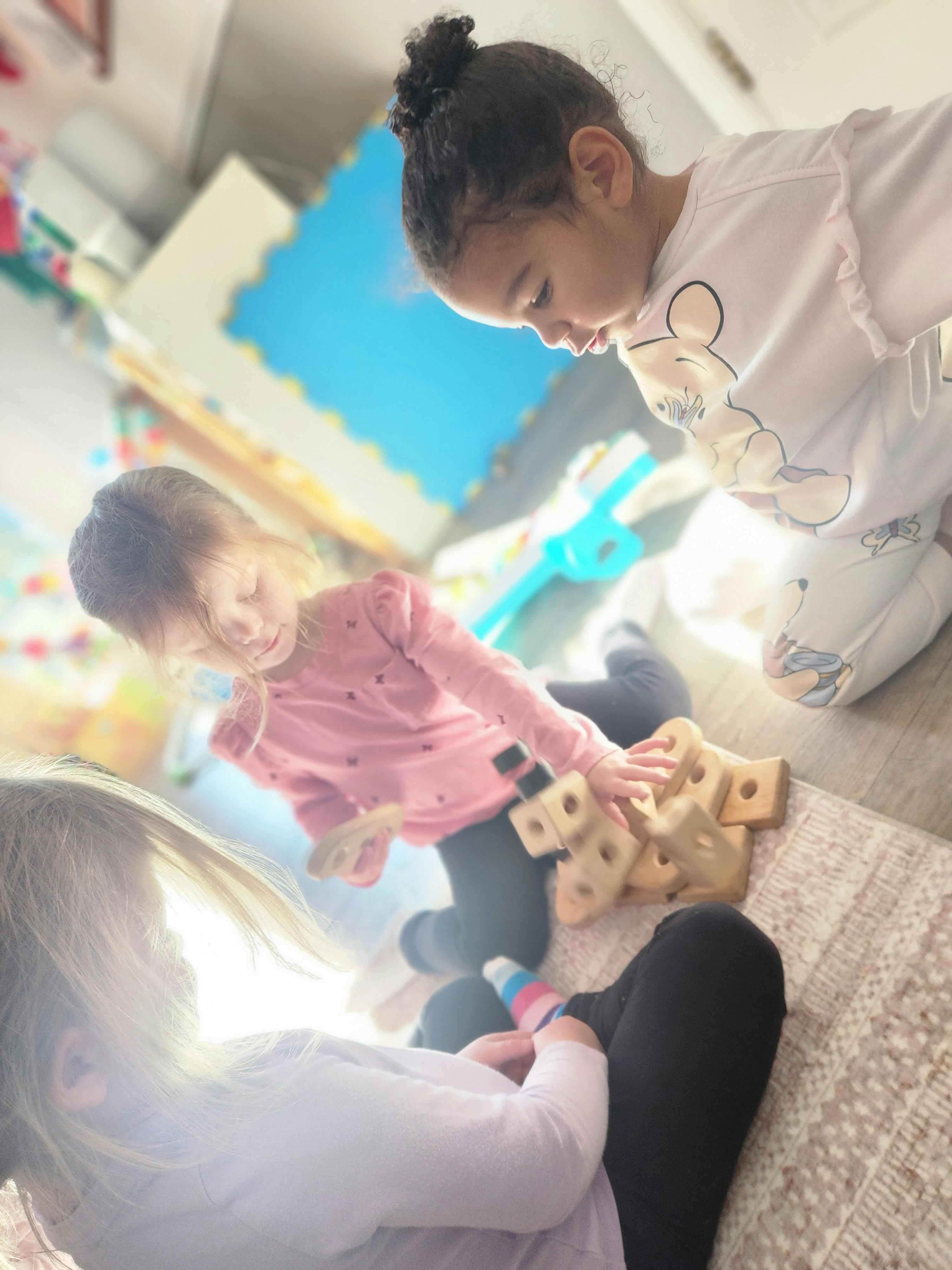 Three children playing with wooden toys on the floor