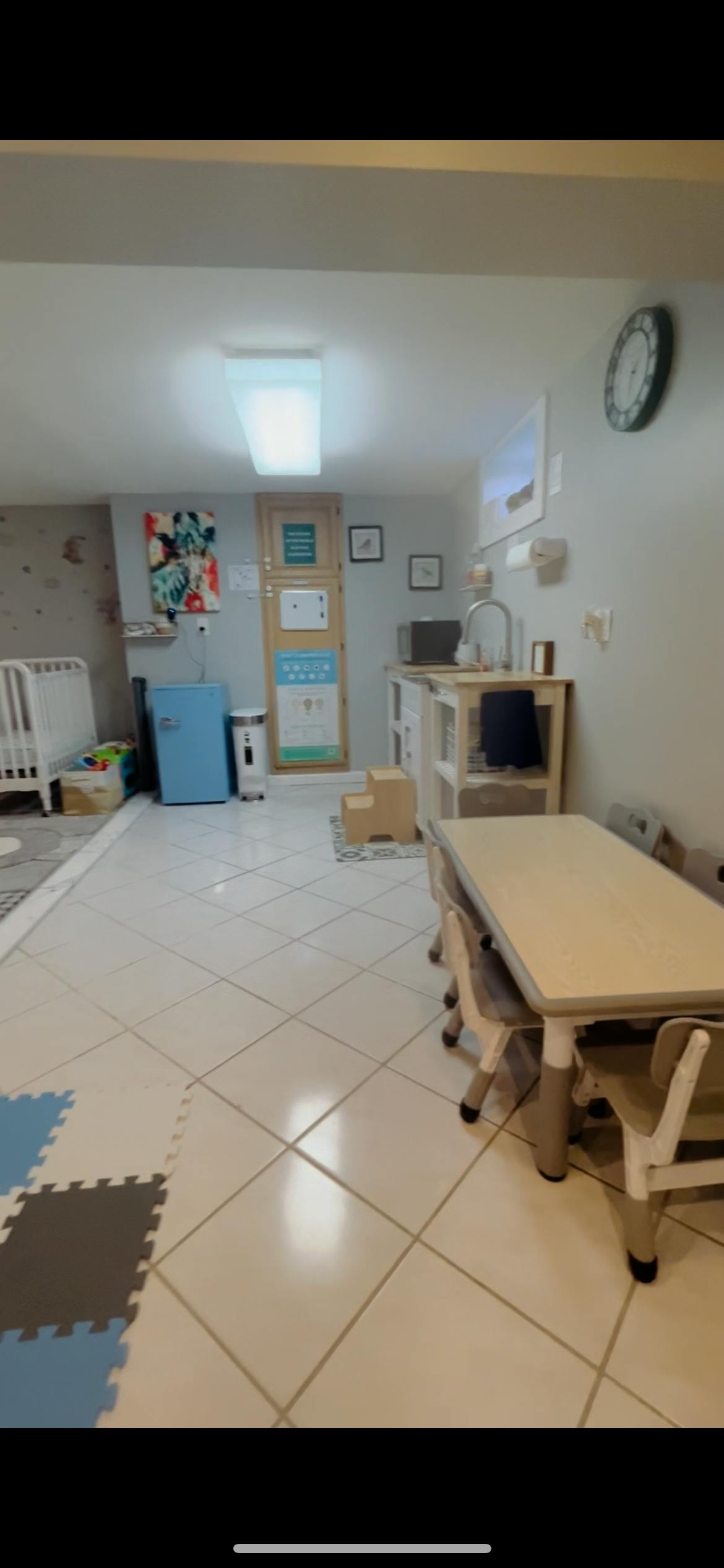 A room with a crib, small table and chairs, and a play kitchen
