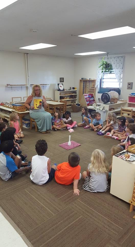 Person reading a book to a group of children in a classroom