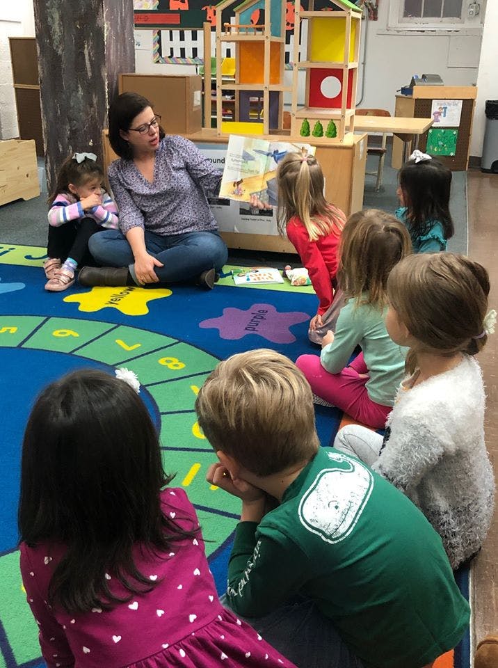 Adult reading a book to children sitting on a rug in a classroom