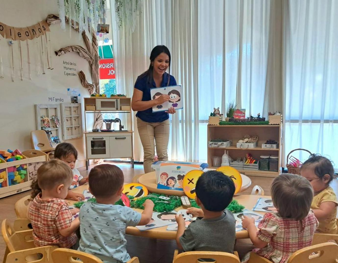 Adult holding a book for children seated at a table in a classroom