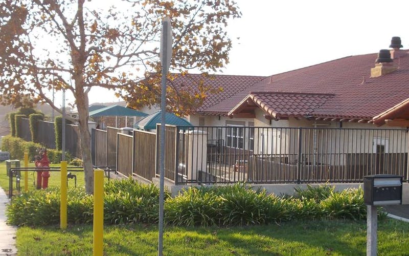 House with a red tile roof, black fence, and green foliage