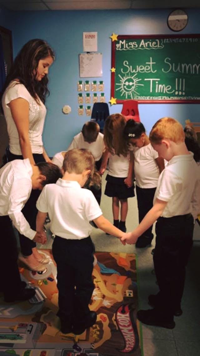 Adult and children holding hands in a circle, heads bowed