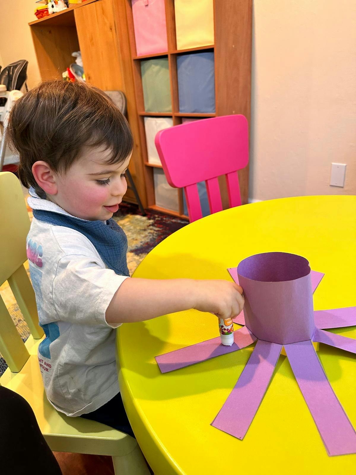 Child crafting with purple paper strips at a table