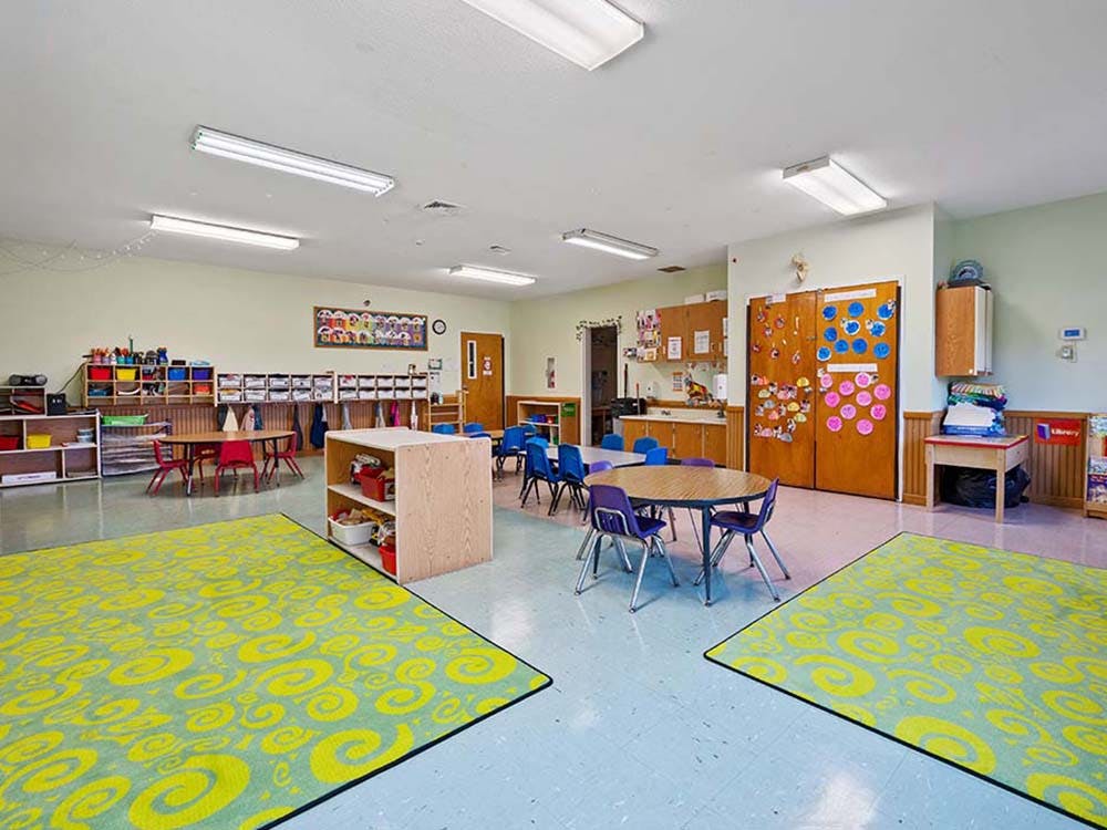 Classroom with small tables and chairs, shelves, and colorful rugs