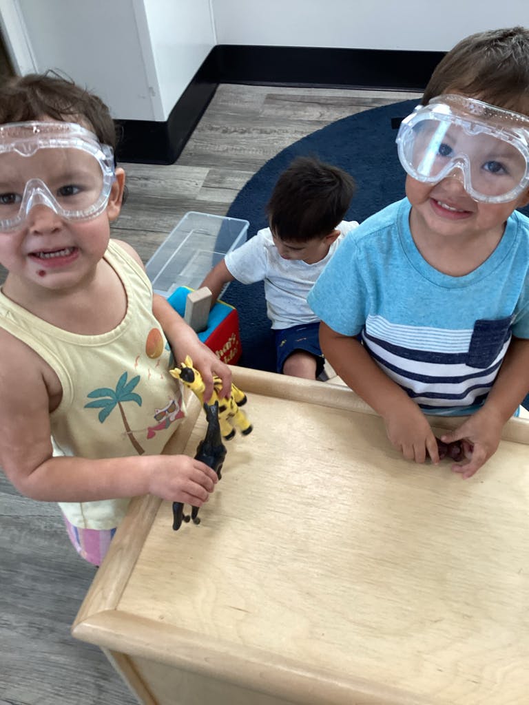 Two children wearing safety goggles playing with toys at a table