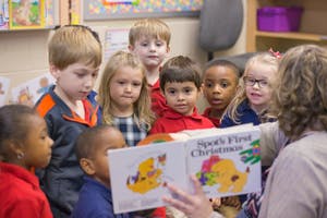 Adult reading a book to a group of children in a classroom