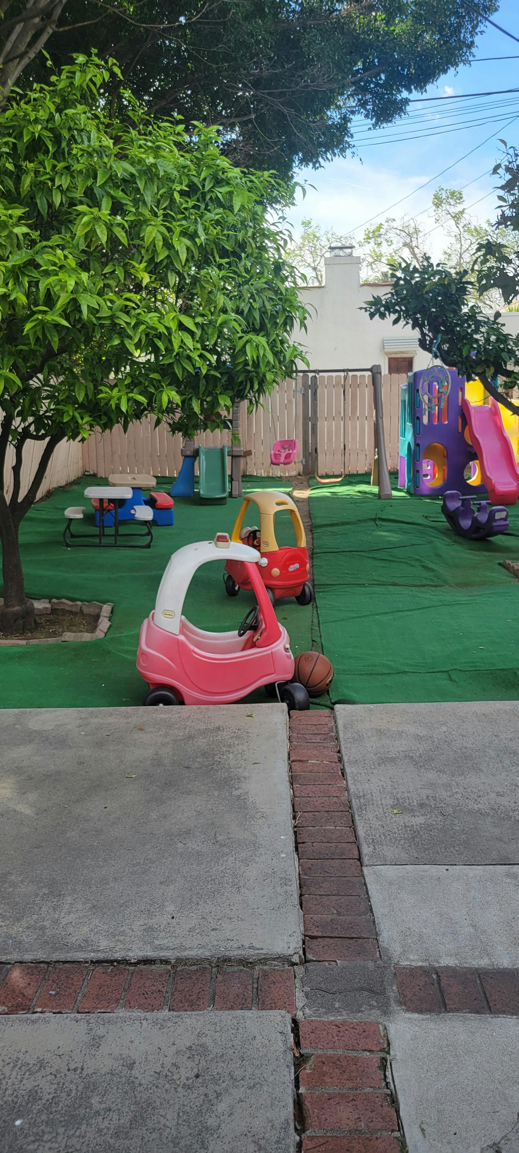 Playground area with small ride-on cars, a plastic slide, and a swing set