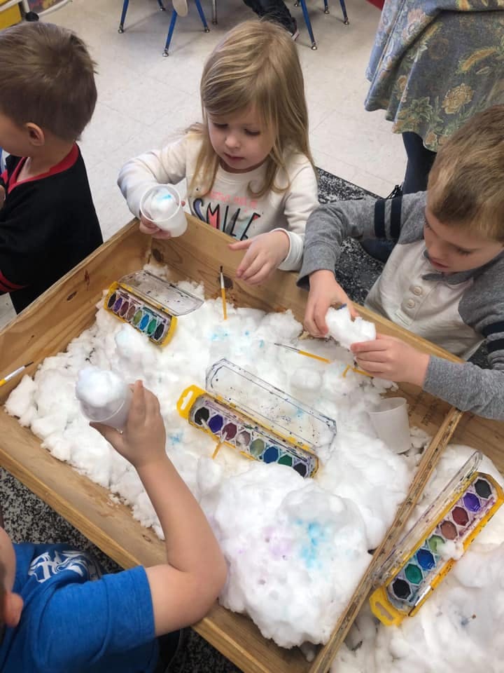 Children playing with paint and cotton in a wooden bin