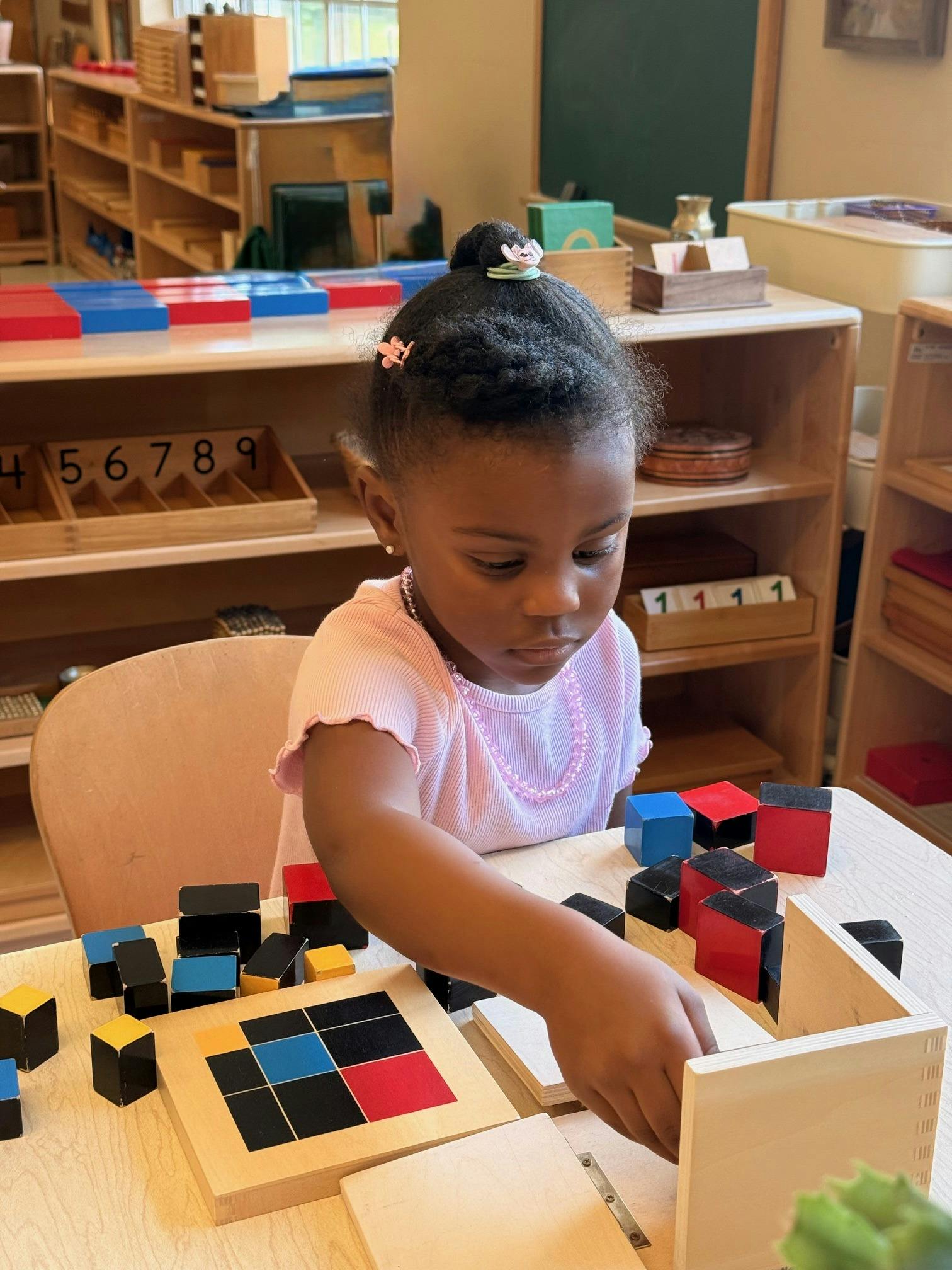 Child playing with colorful blocks at a wooden table in a classroom