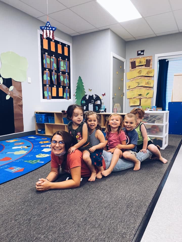 Person lying on floor with four children sitting on their back in a classroom