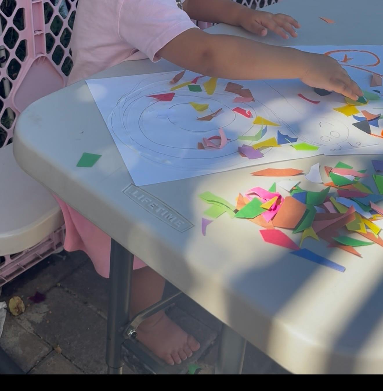 Child gluing paper pieces onto a drawing on a table