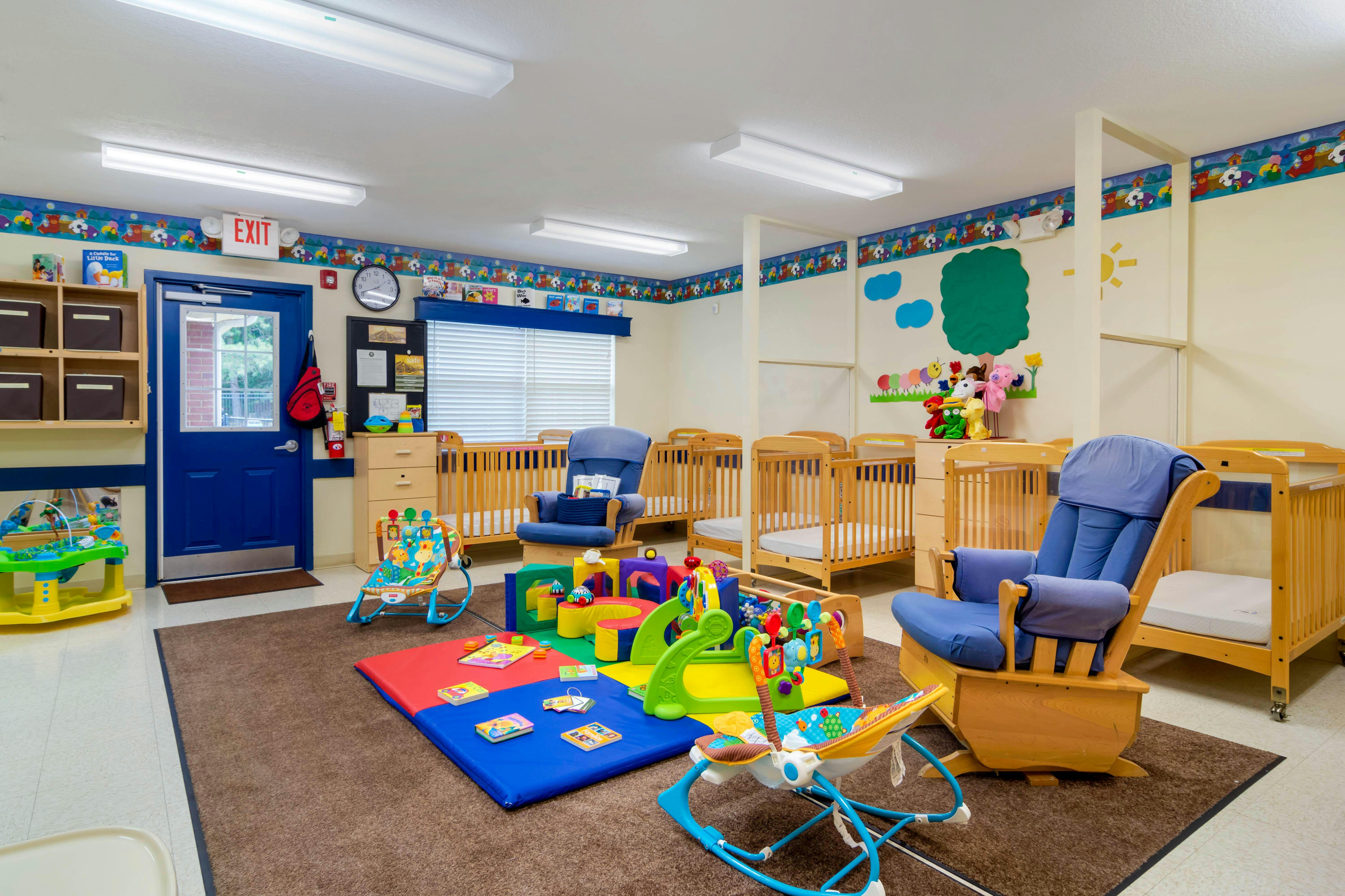 A colorful childcare room with cribs, play mats, and a rocking chair