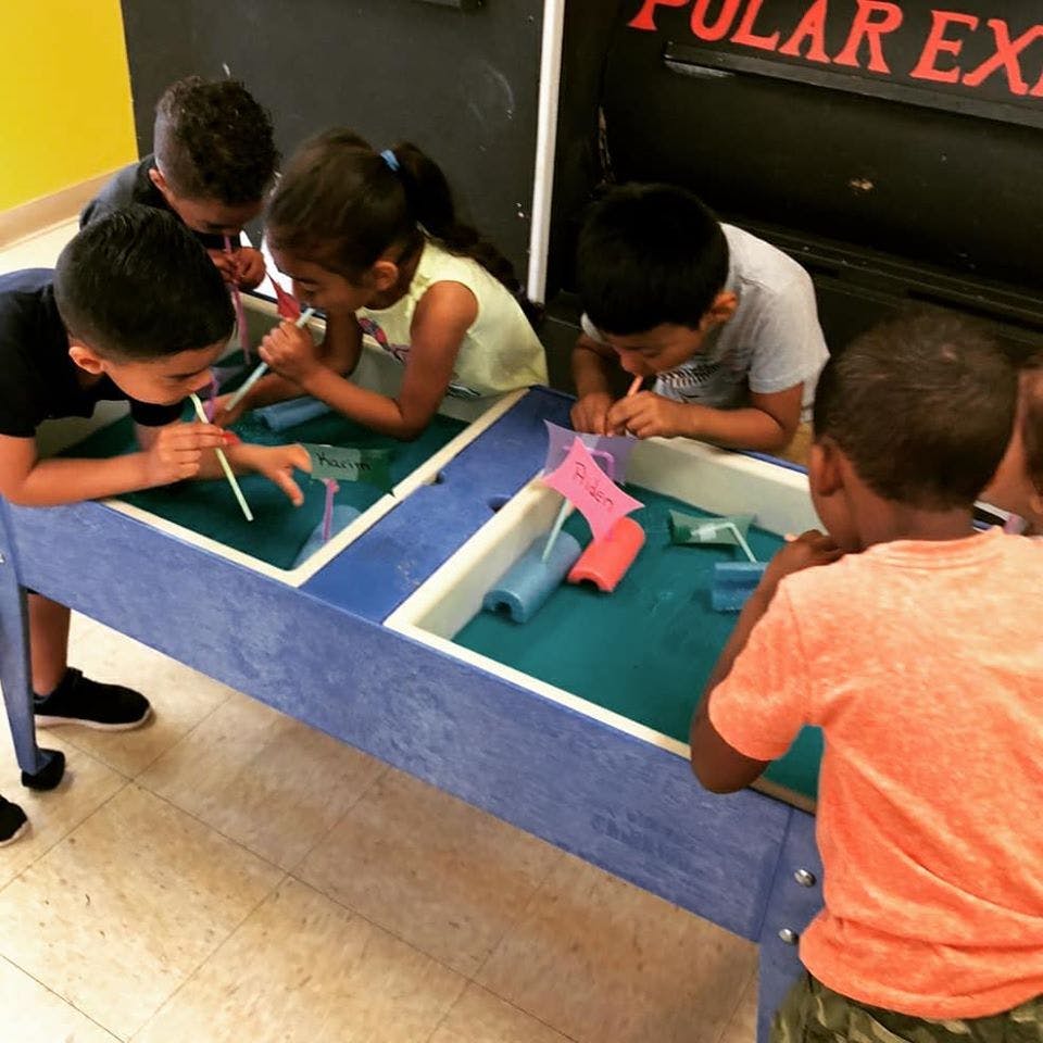 Children blowing through straws into water at a water table