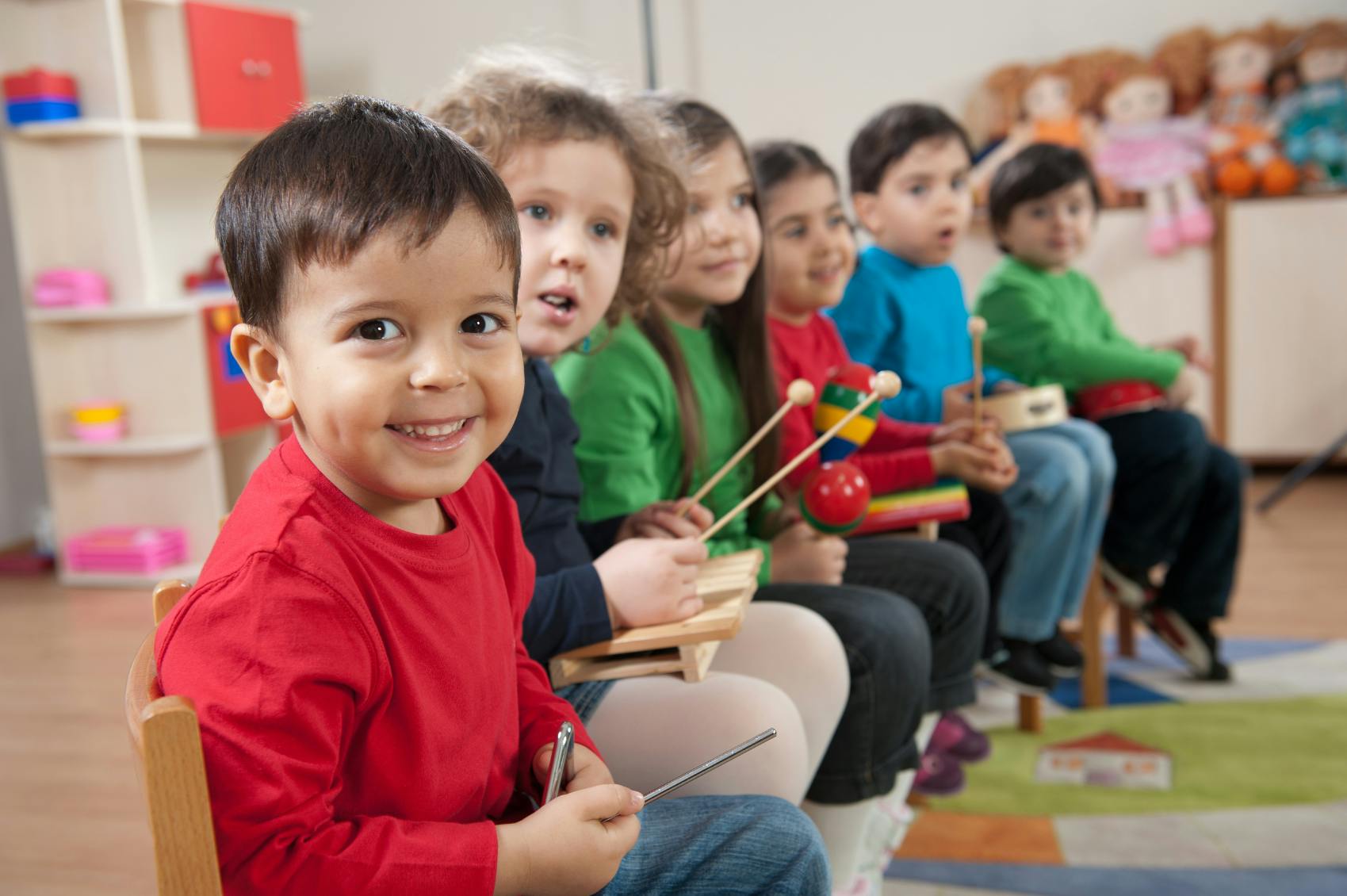 Children sitting in a row, some holding musical instruments