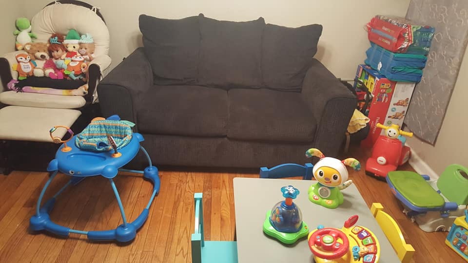 Living room with a dark sofa, baby bouncer, walker, and various toys