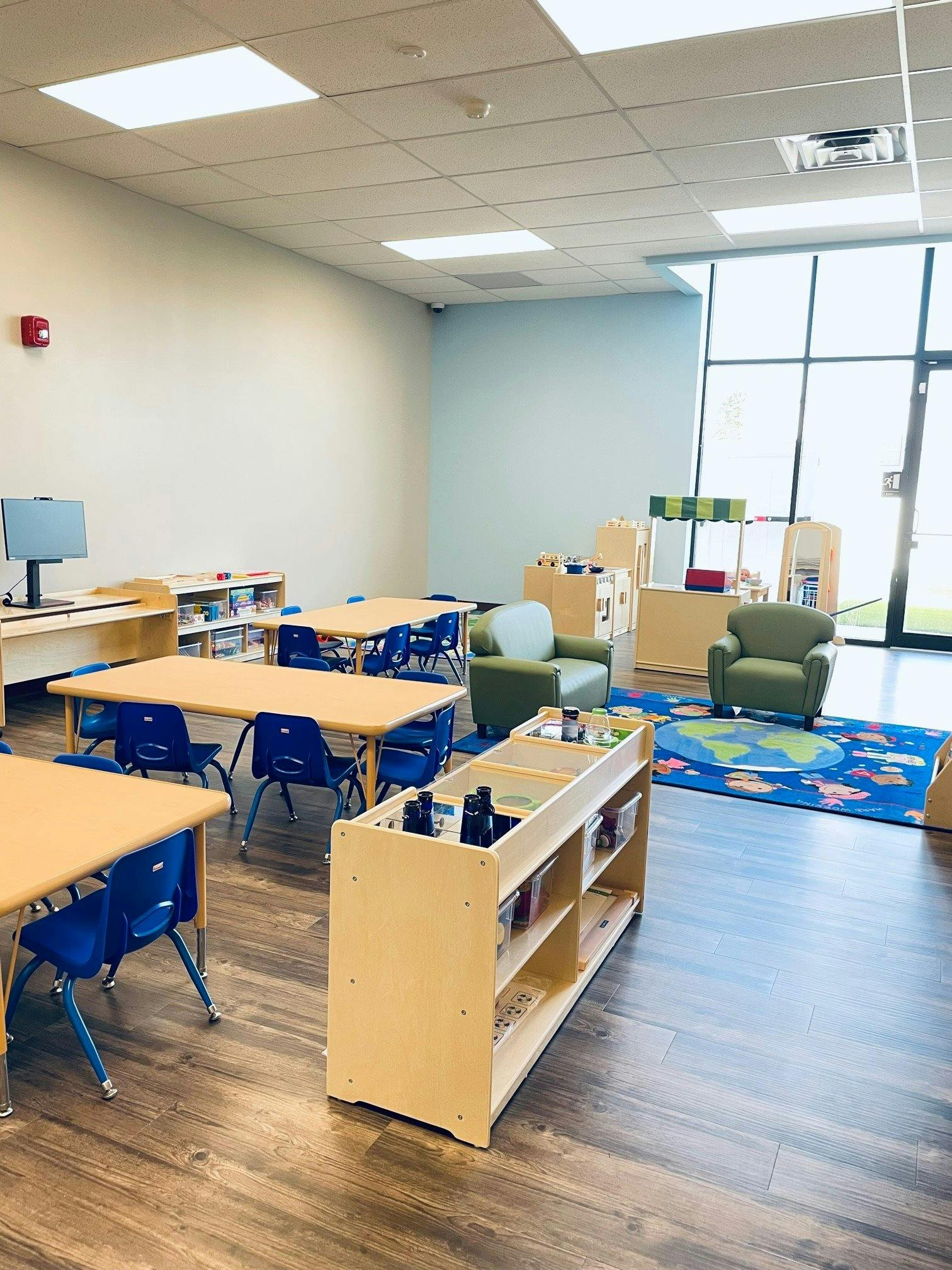 Classroom with small tables and chairs, two armchairs, and a world map rug