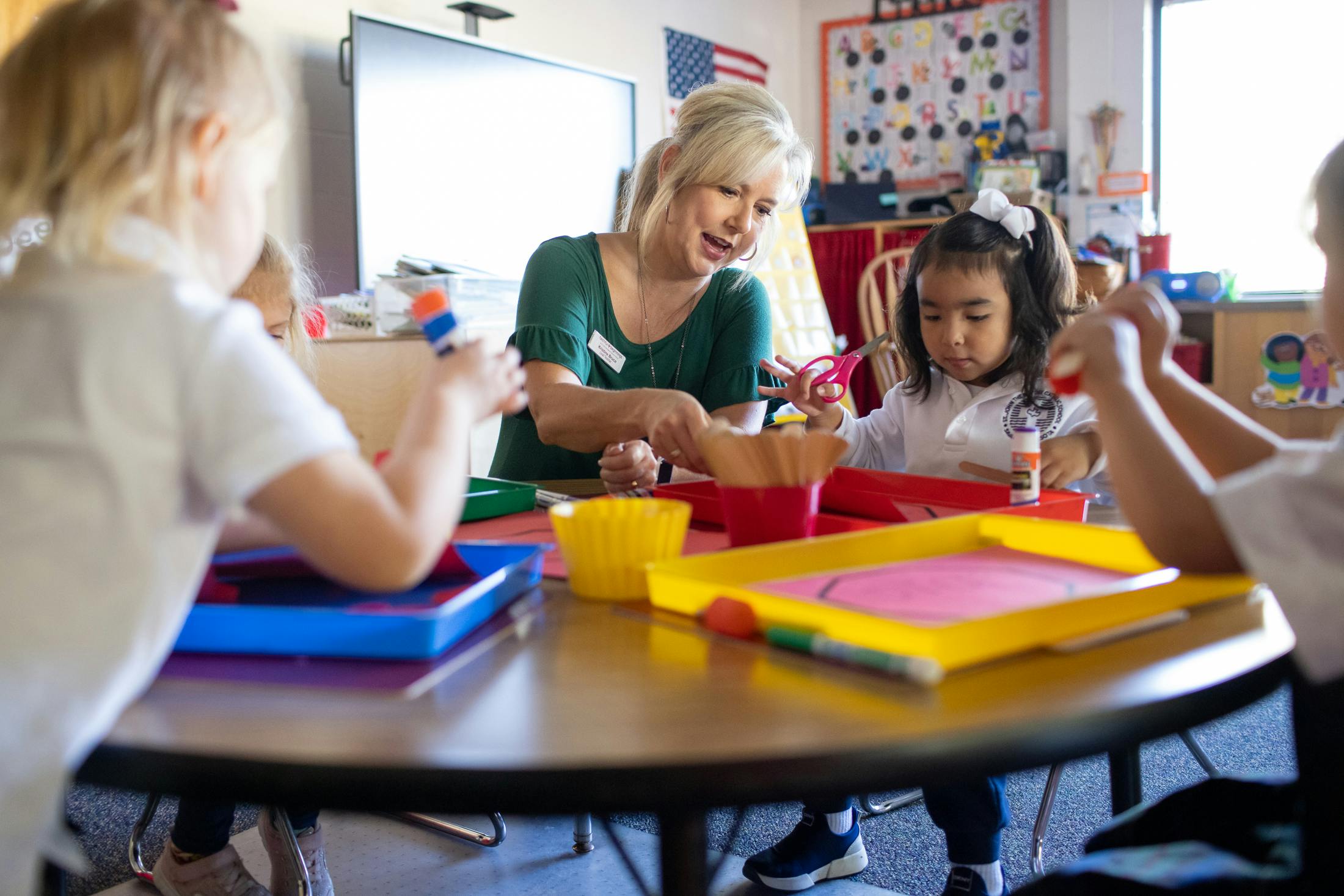 Adult and children doing crafts at a table in a classroom