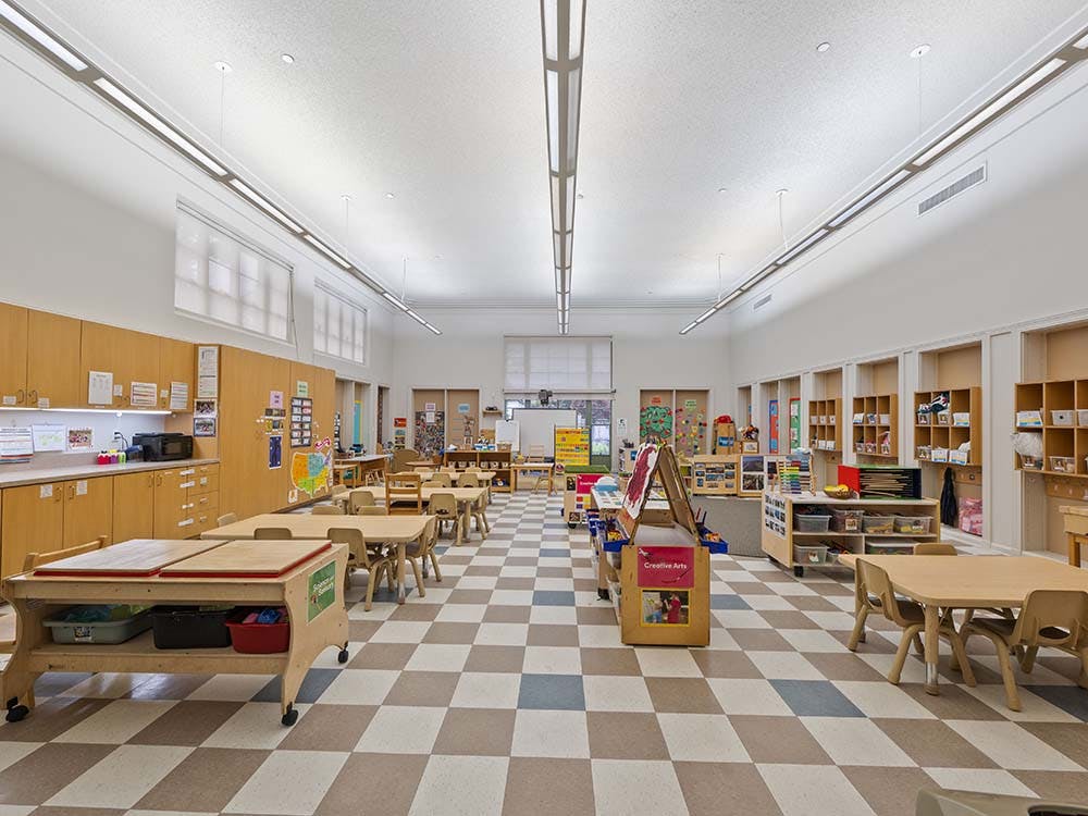 Empty classroom with small tables and chairs, shelves, and learning stations