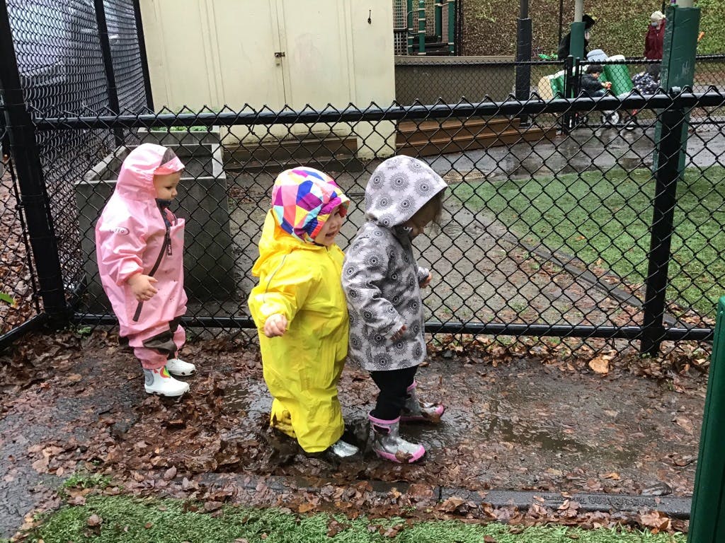 Three children in rain gear standing by a fence