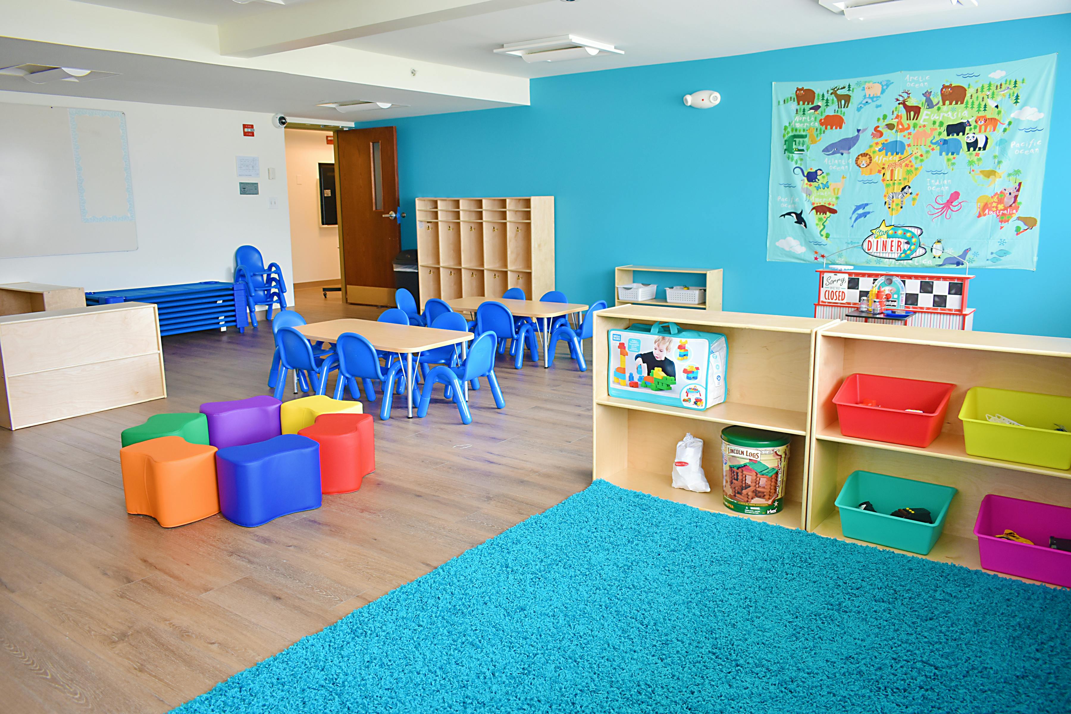 Classroom with small tables and chairs, colorful soft blocks, and shelves