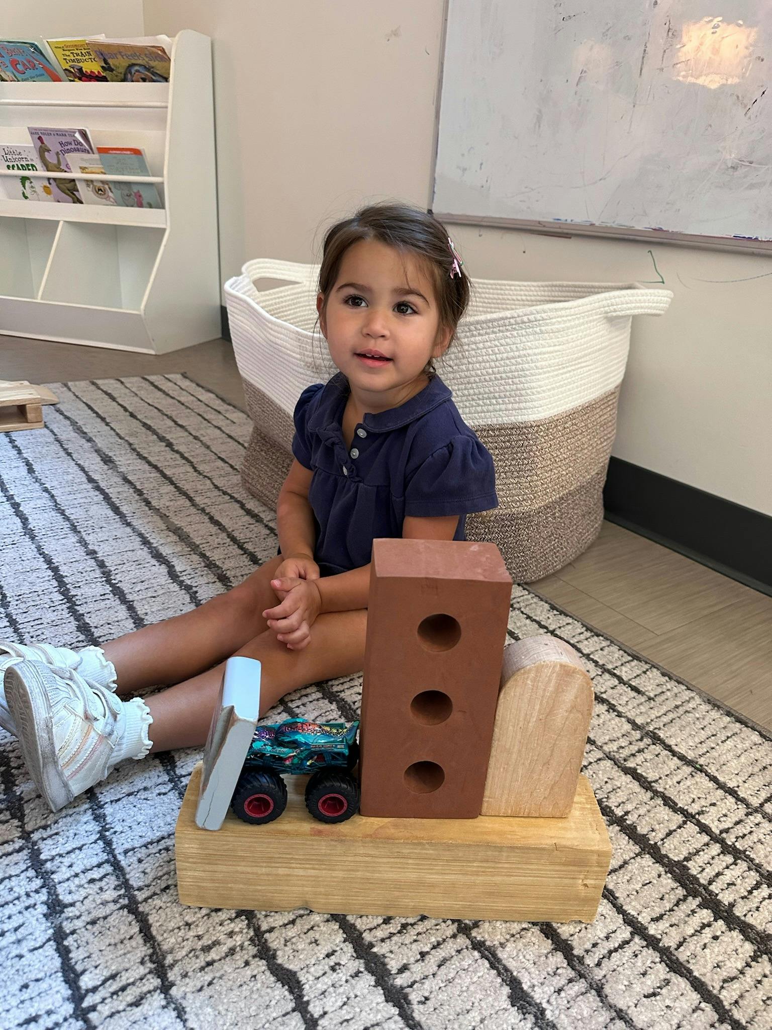 Child sitting on a rug playing with blocks and a toy vehicle