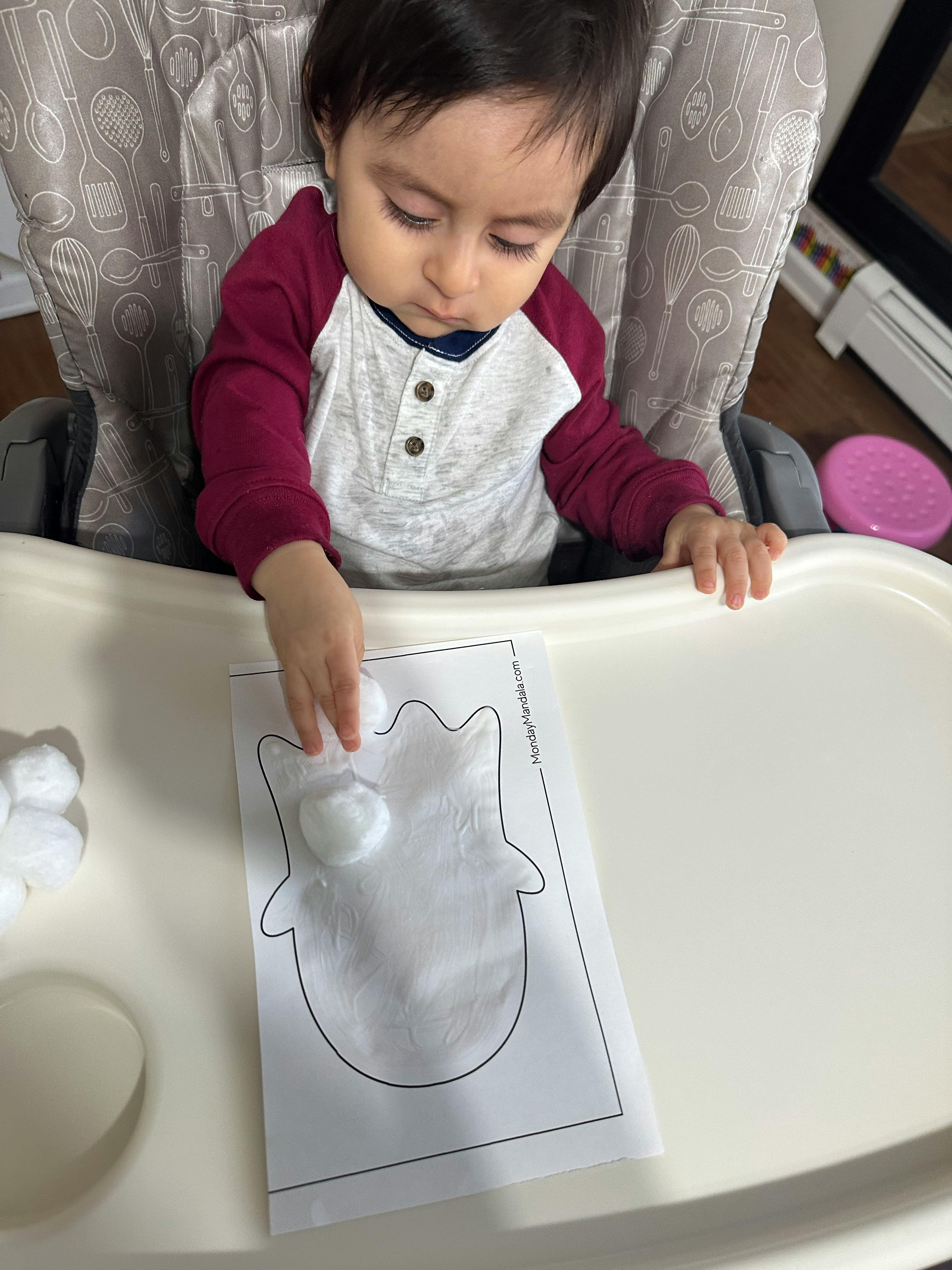 Child in high chair placing cotton balls on a paper cutout