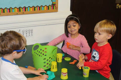 Three children playing with modeling clay at a table