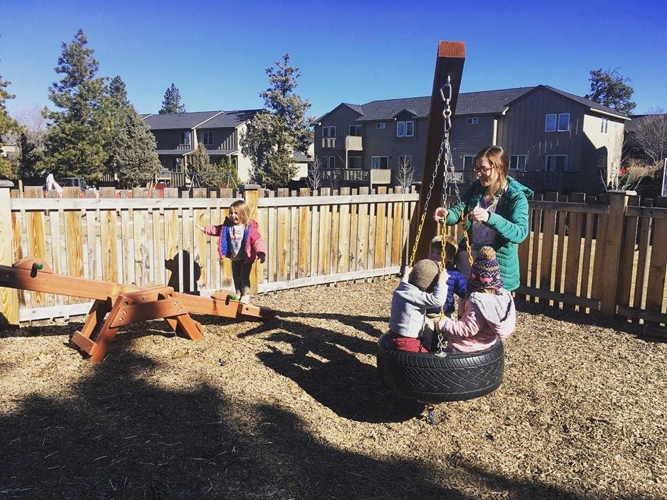 Person with two children on a tire swing and a child near a seesaw in a playground