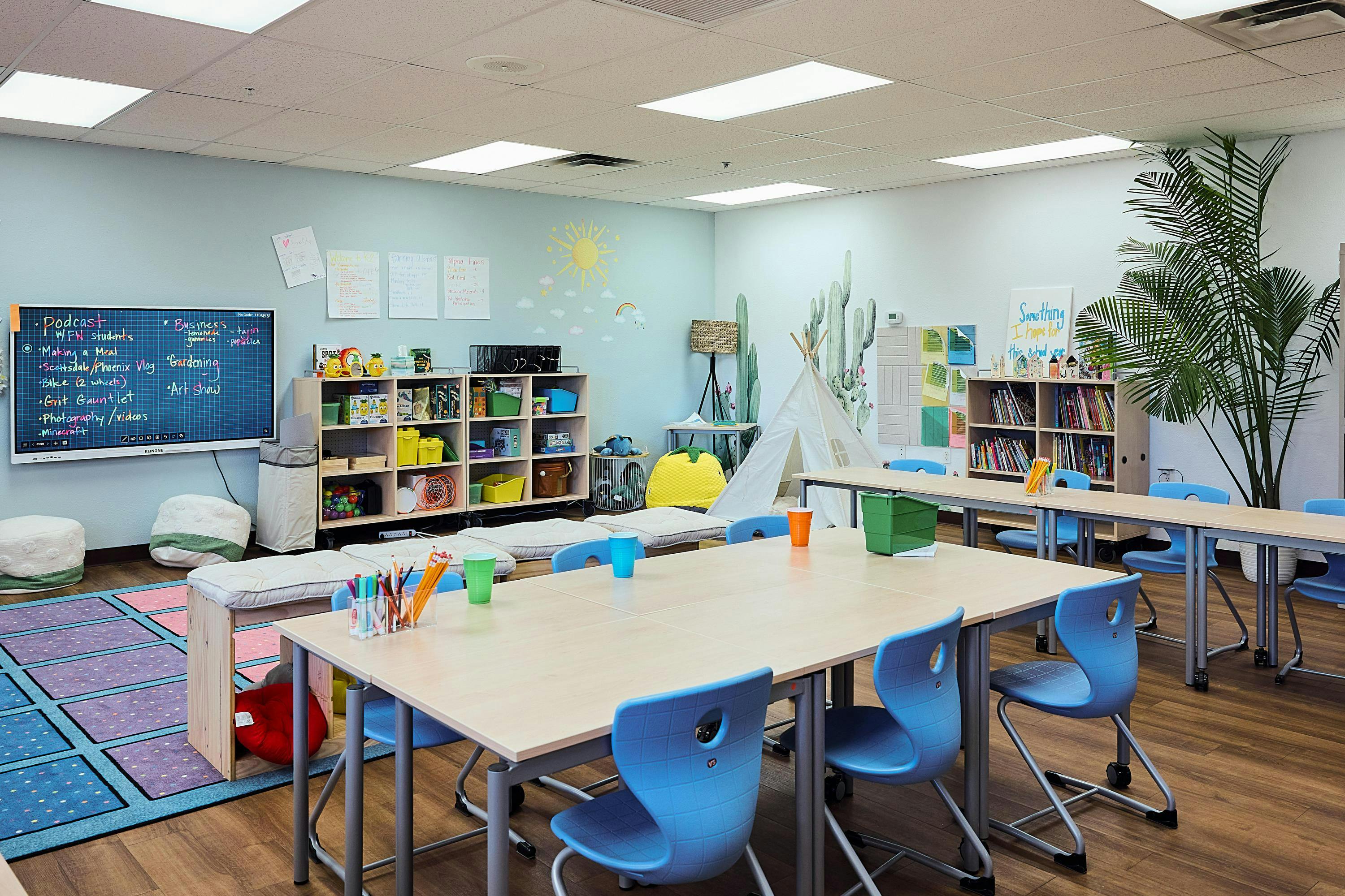 Classroom with tables, blue chairs, shelves, and a large interactive whiteboard