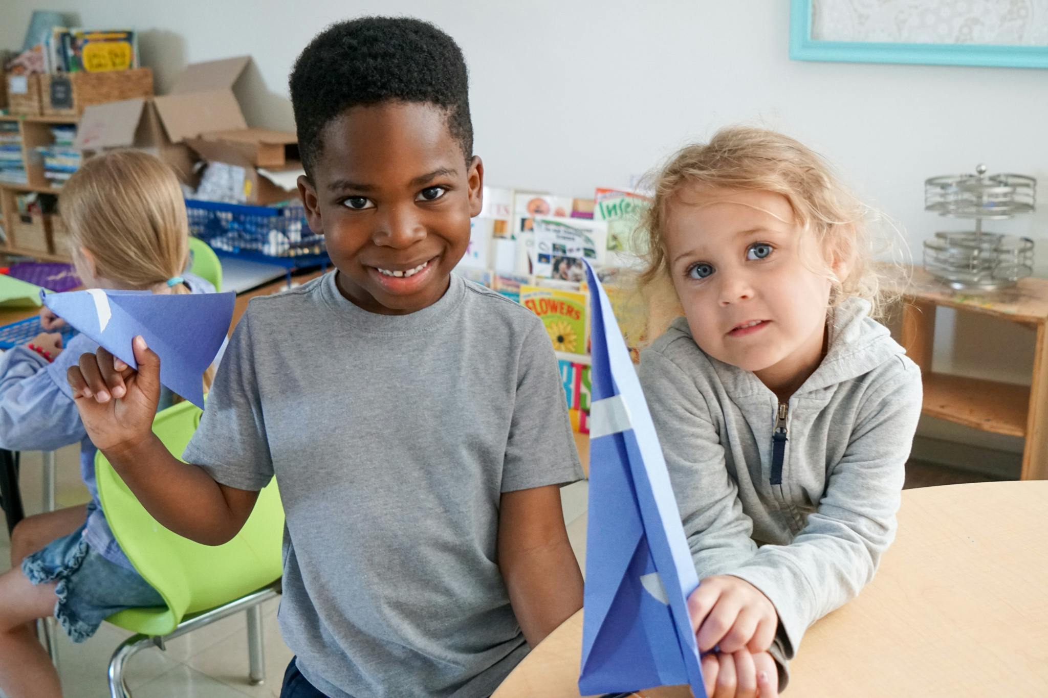 Two children holding blue paper airplanes in a classroom