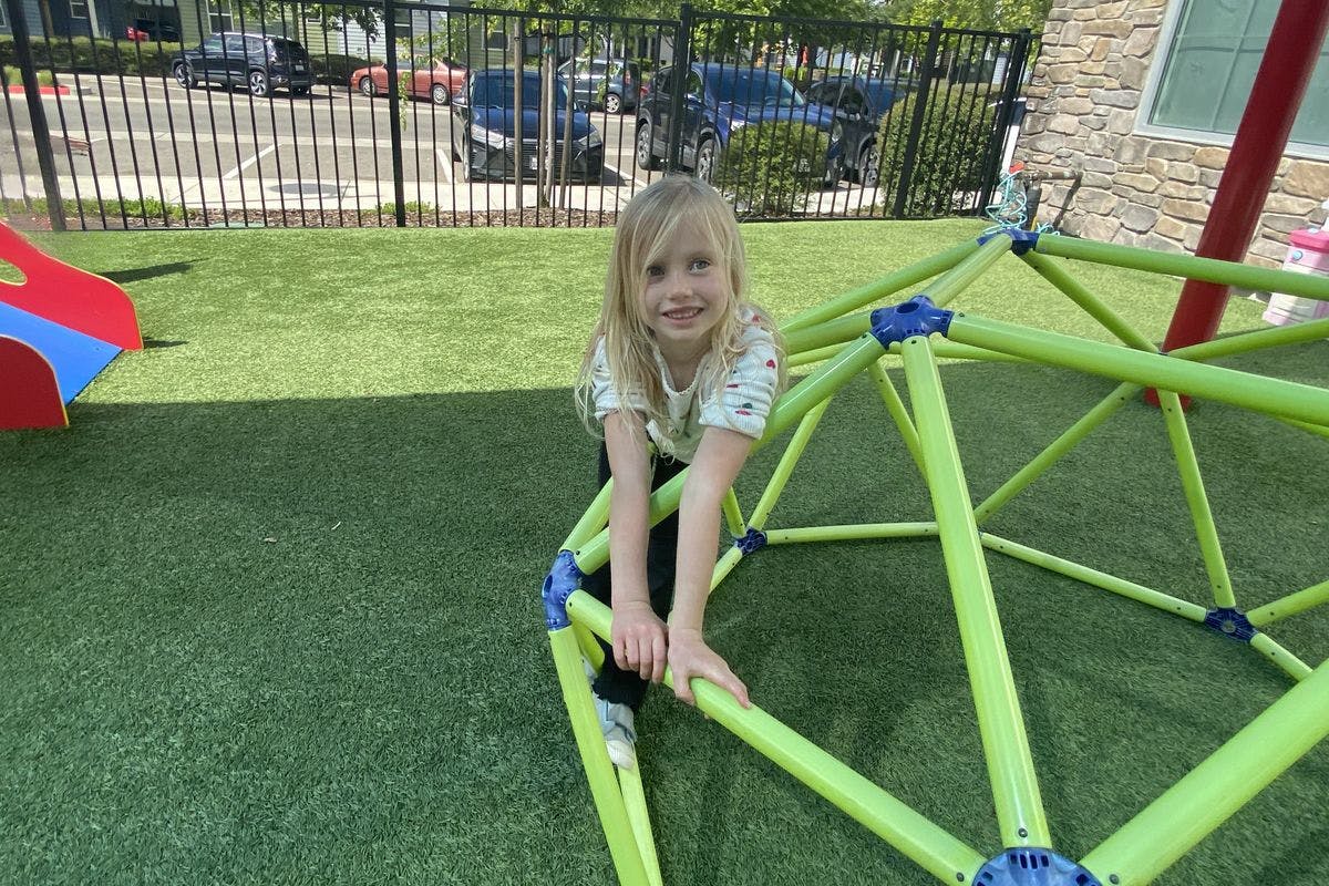 Child smiling while climbing on a geodesic dome in a playground