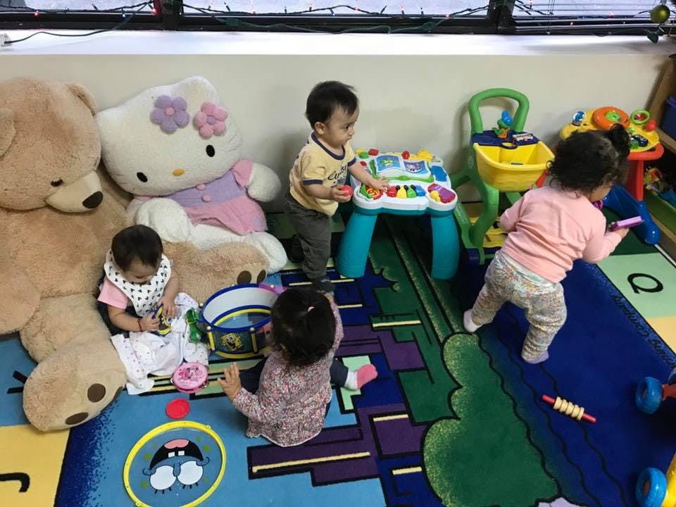 Multiple children playing with toys and stuffed animals on a colorful rug