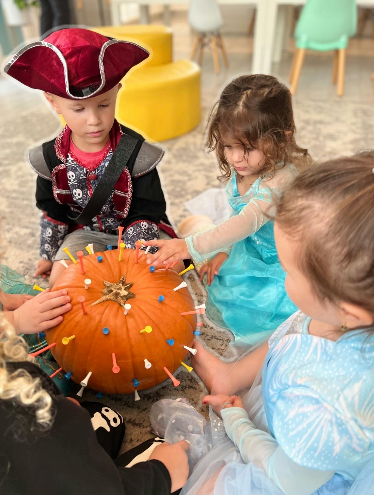 Children in costumes putting golf tees into a pumpkin
