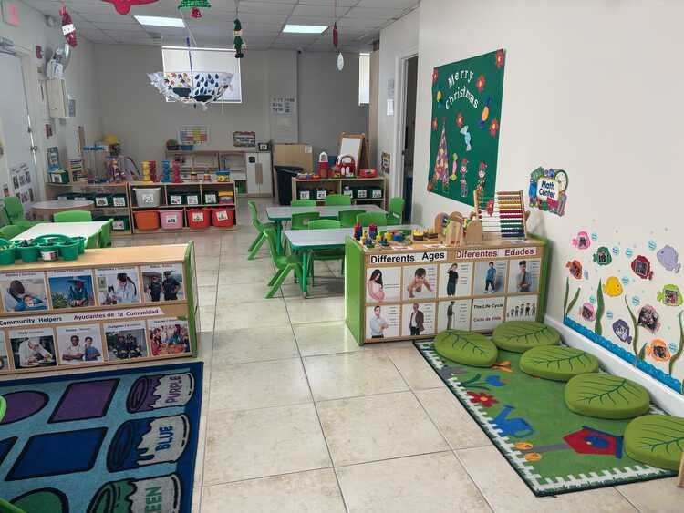 Classroom with small tables and chairs, shelves with books and toys