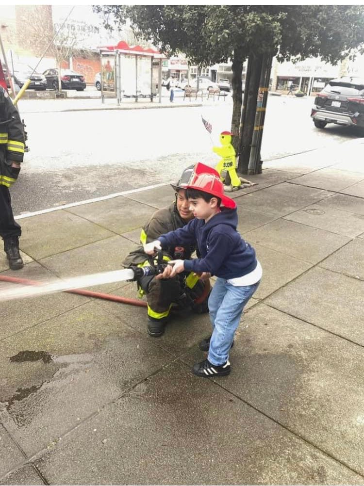 Firefighter helping a child hold a fire hose