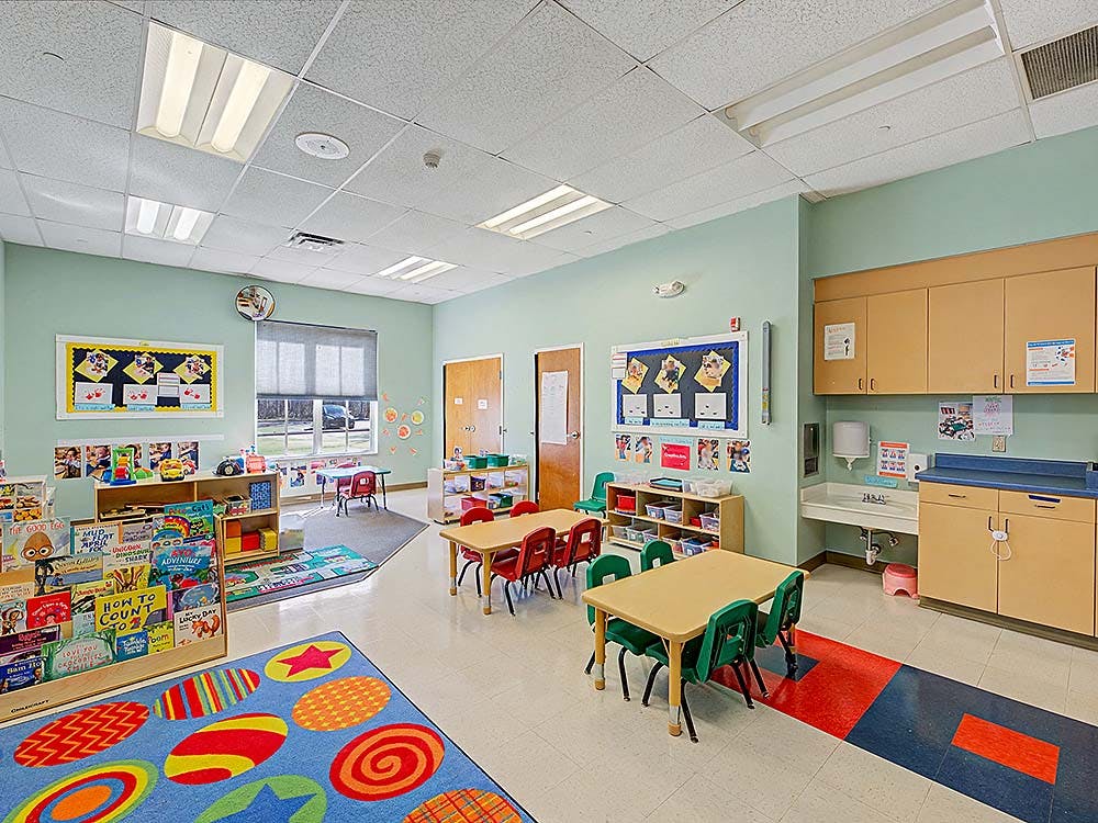 Classroom with small tables and chairs, a sink, and a bookshelf with books
