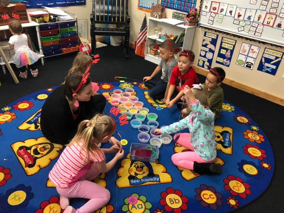 Adult and children sitting on a rug playing with colorful containers