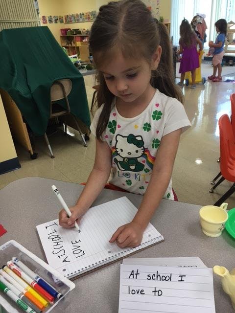 Child writing on paper at a table in a classroom