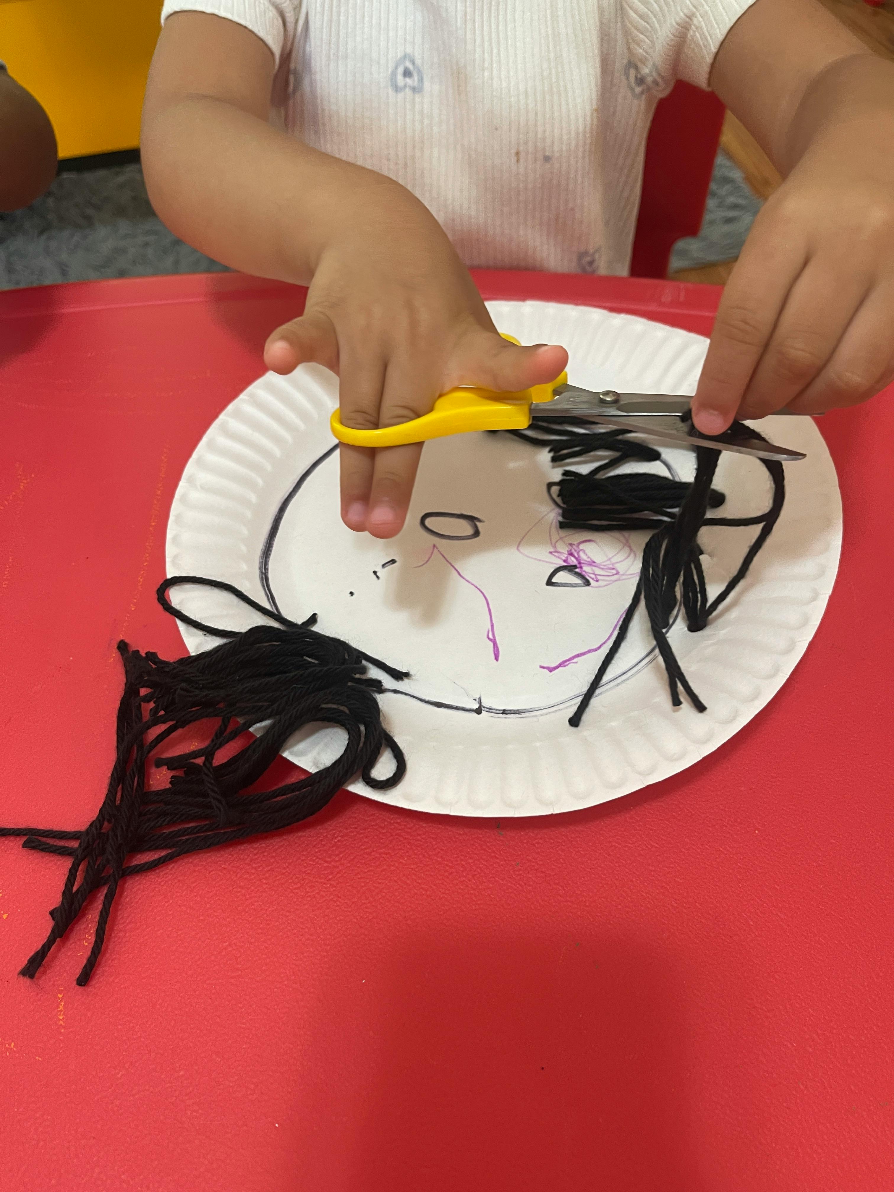 Child cutting yarn on a paper plate craft