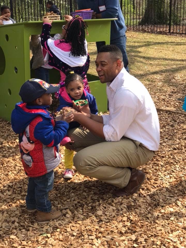 Adult person crouching and interacting with two children outdoors
