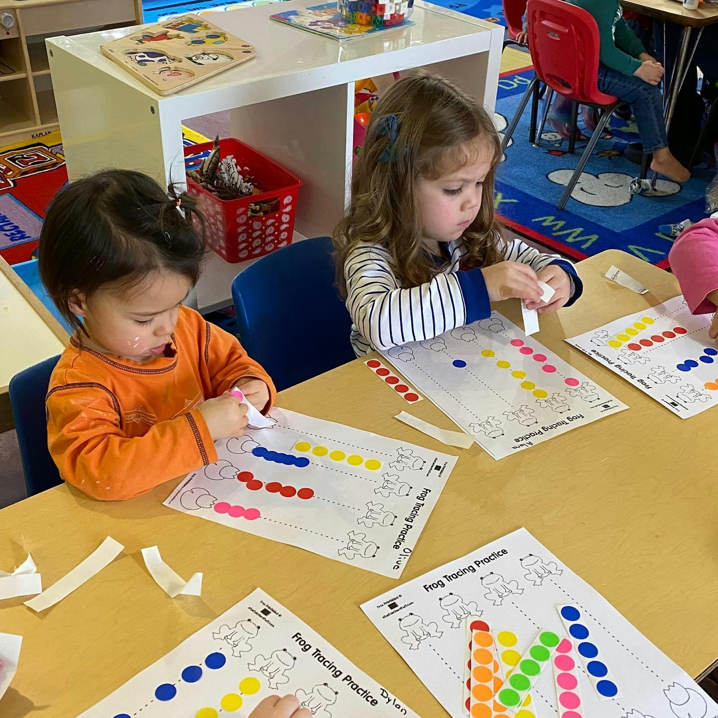 Two children placing colorful stickers on papers at a table