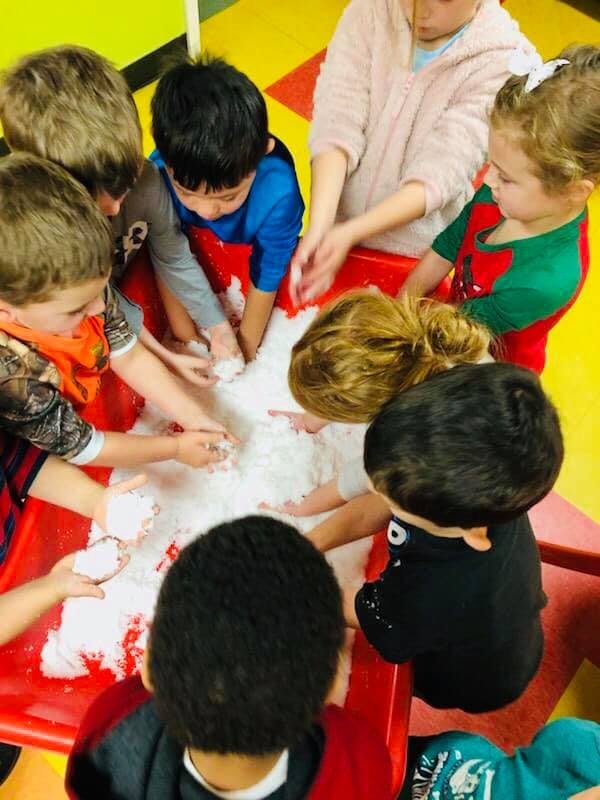 Children playing with white sensory material in a red bin