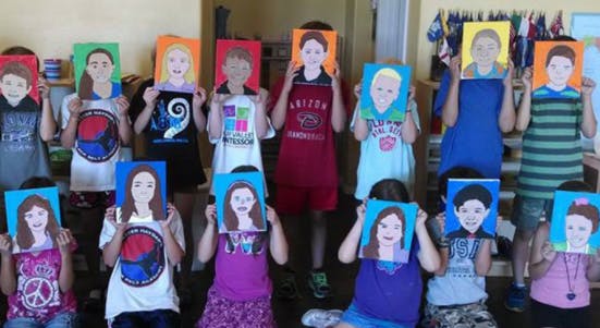 Group of children holding up self-portrait paintings in front of their faces