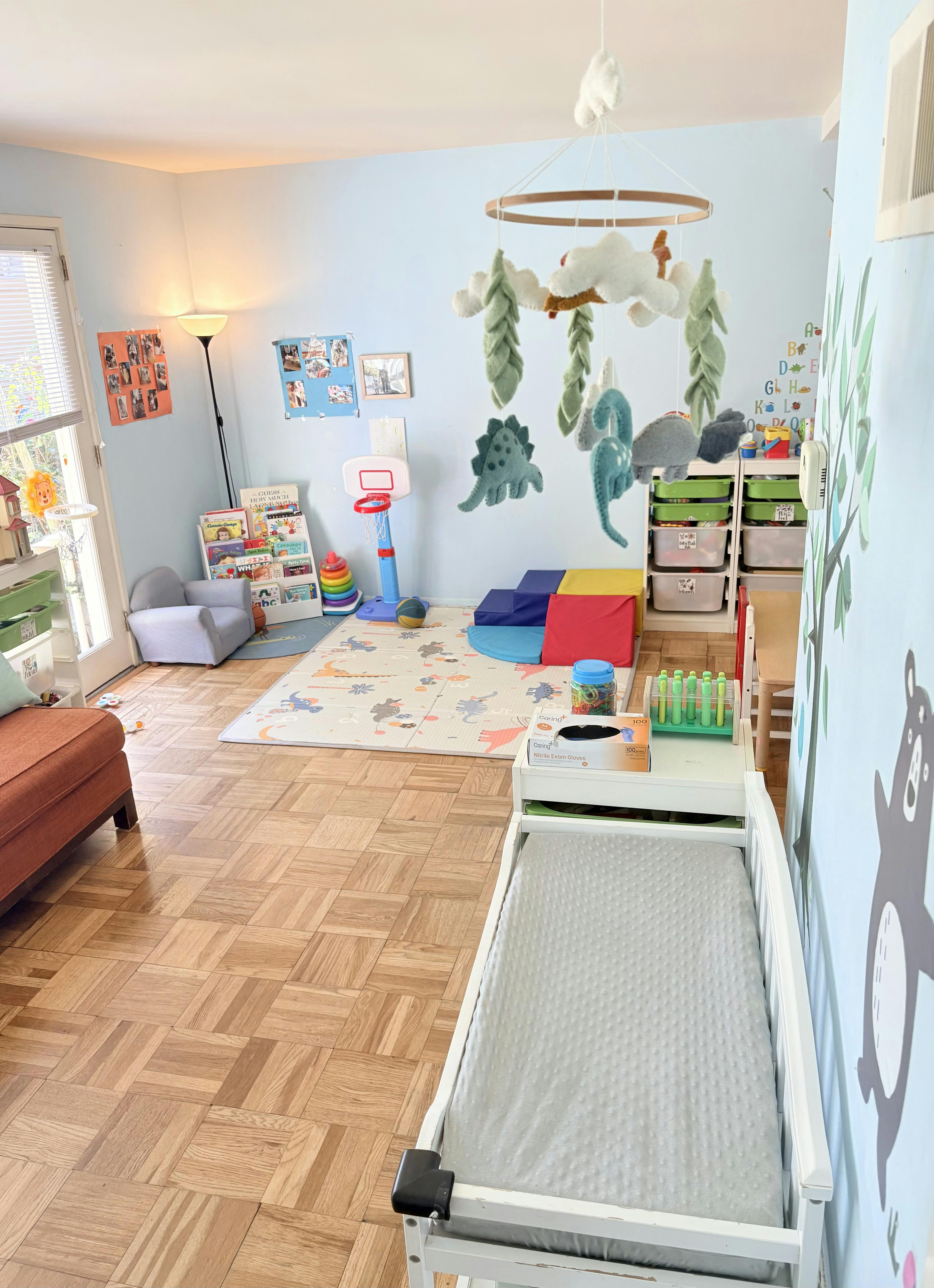 A playroom with a changing table, padded floor mat, shelves of toys, and books