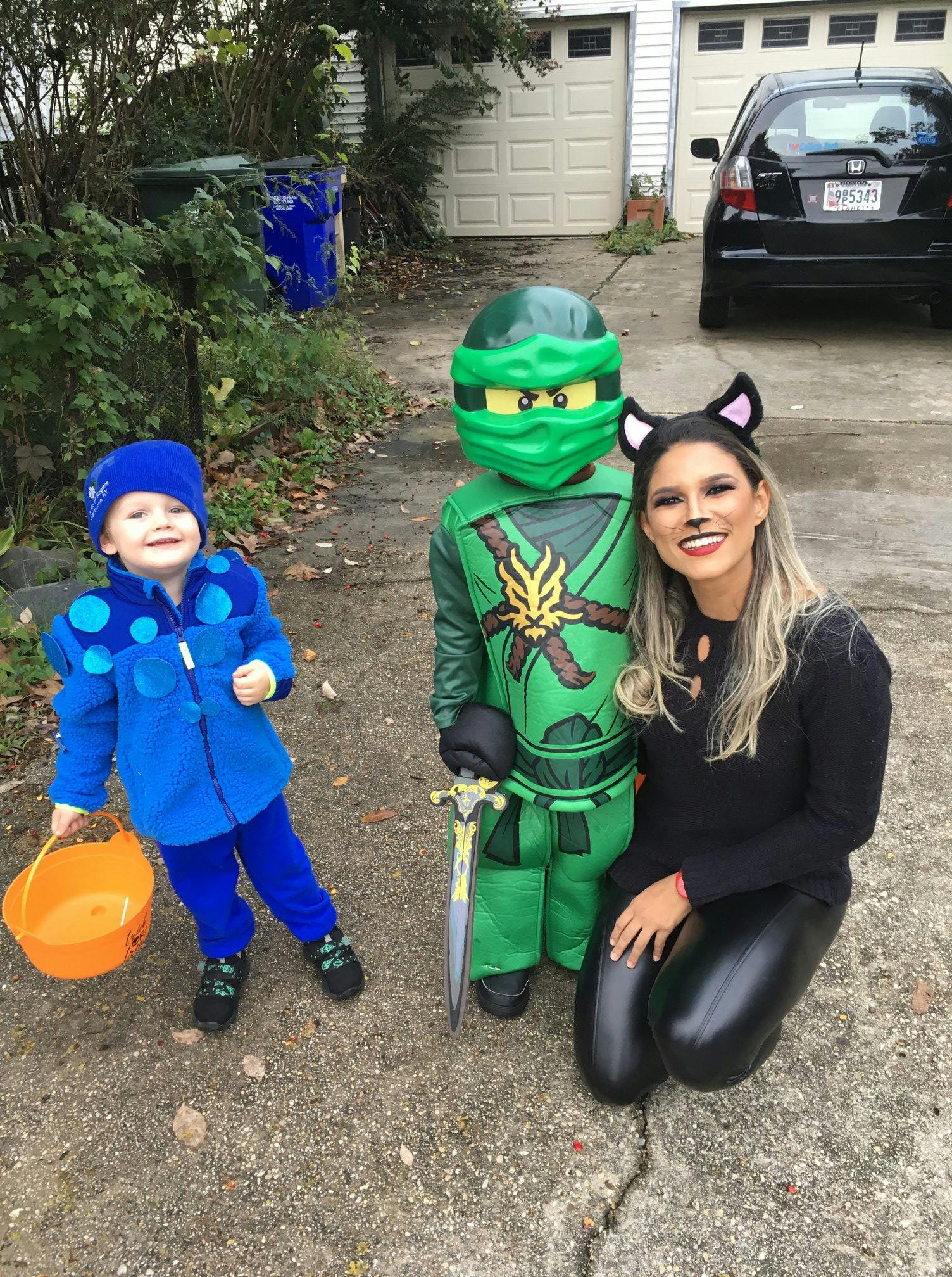 Person in cat costume kneeling next to child in green ninja costume and child in blue costume