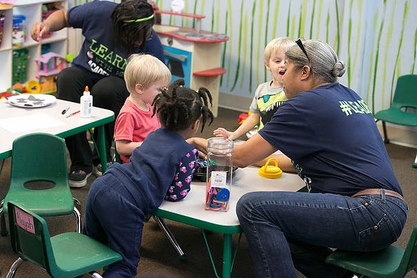 Adults and children at small tables in a classroom